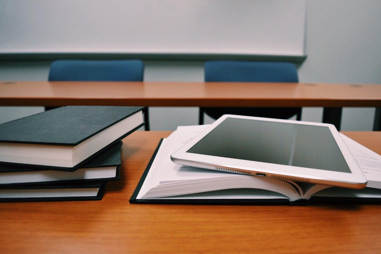 Accueil Books and a tablet on a desk in a classroom, depicting modern education.